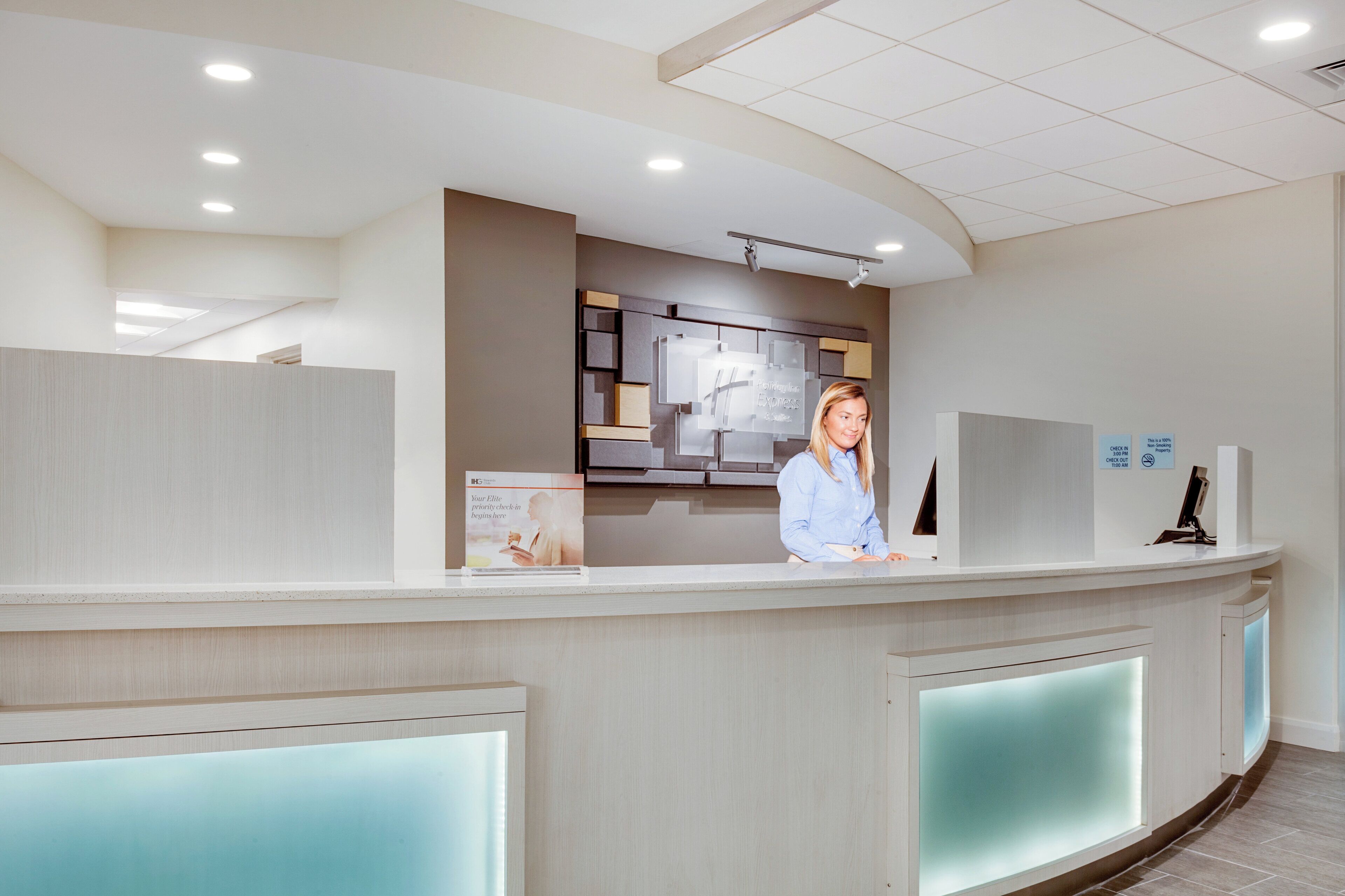Ein modern gestalteter Hotel-Empfangsbereich mit Empfangstresen, einem digitalen Bildschirm und einer Anzeige der Check-in-Zeiten.
