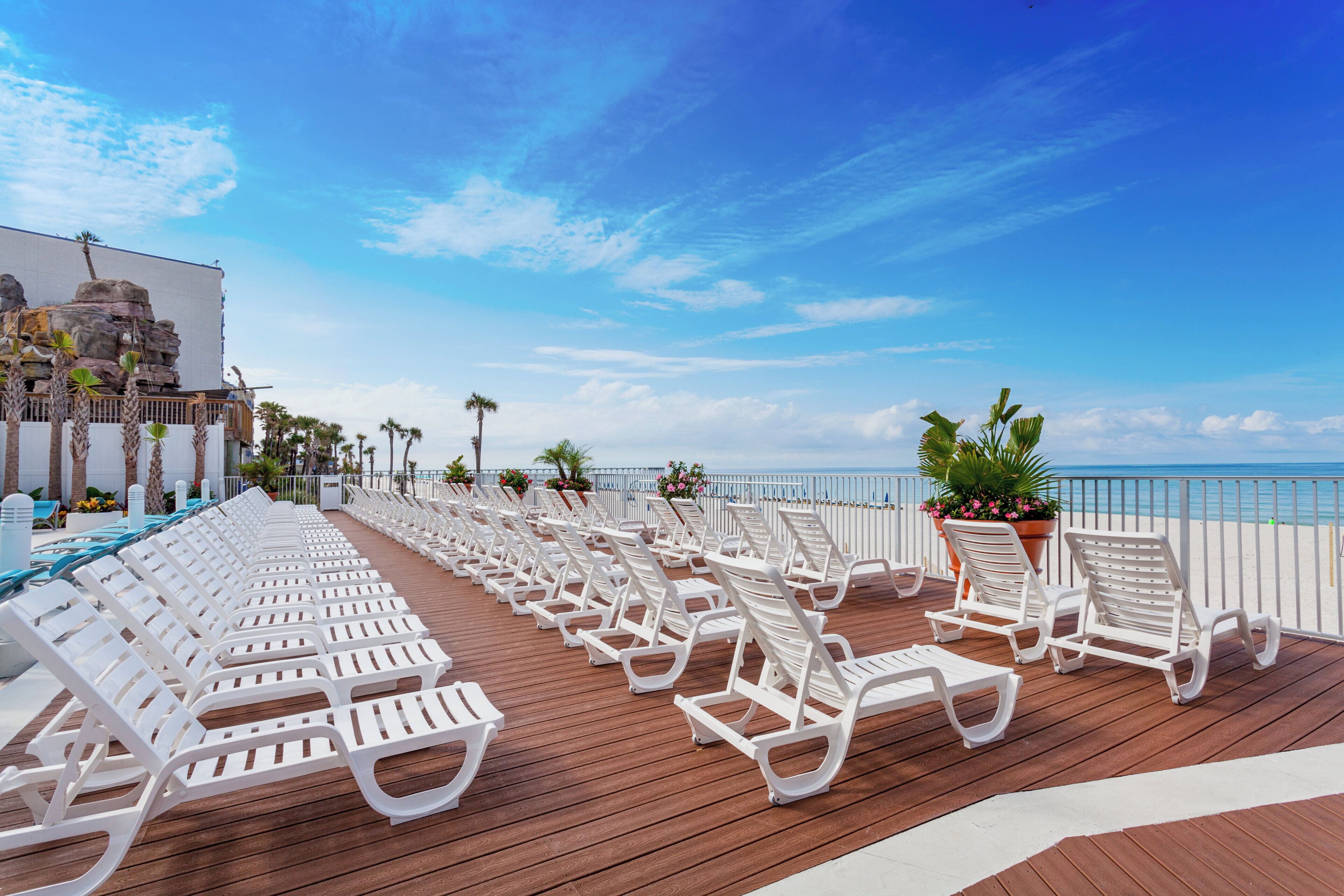 Una terraza con sillones blancos para tomar el sol, con vista a una playa y al océano.
