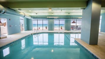 An indoor swimming pool with clear views of the ocean, large windows, and a ceiling with air ducts.