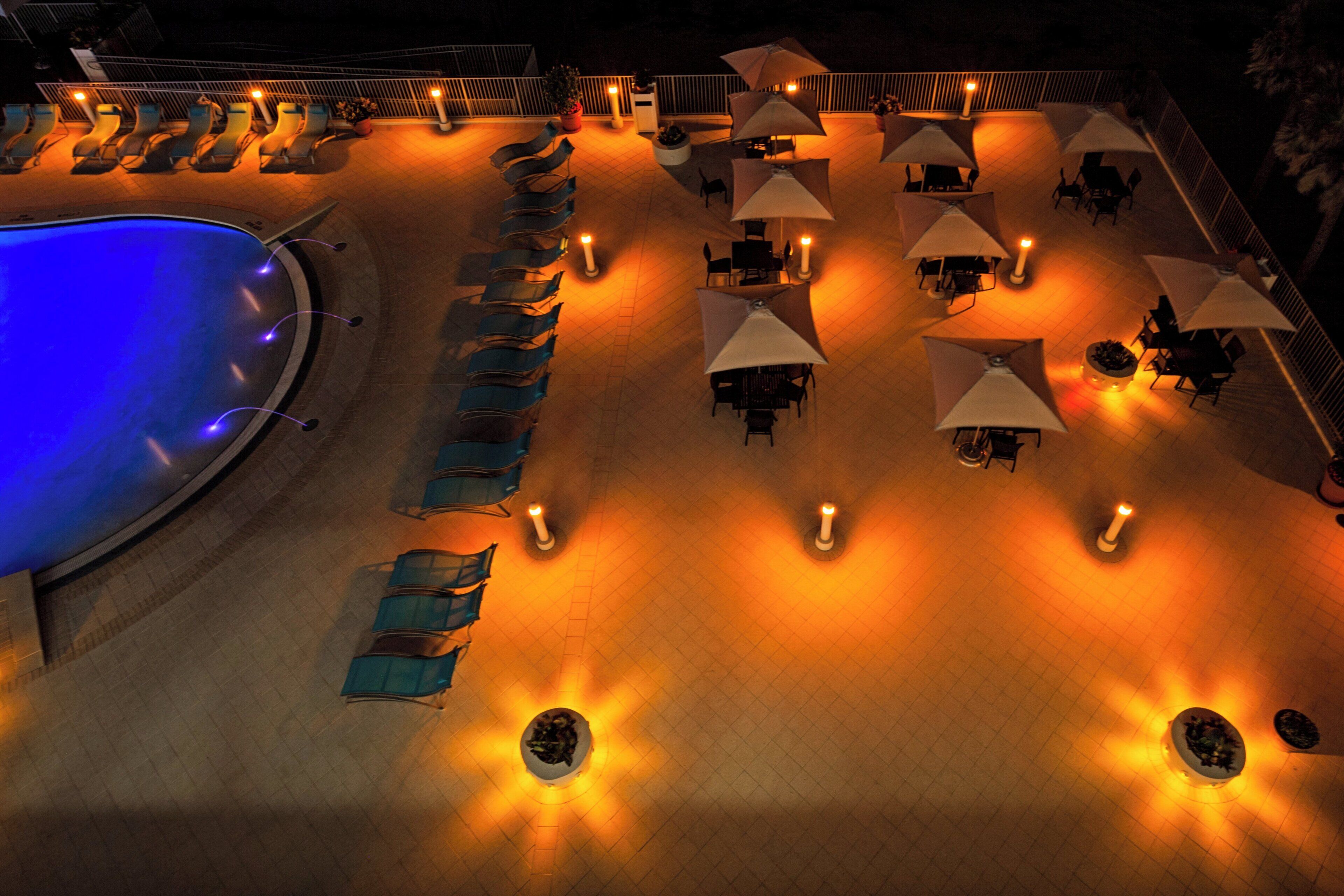Zona de piscina con sillones de descanso y sombrillas, una piscina y suelo de baldosas.