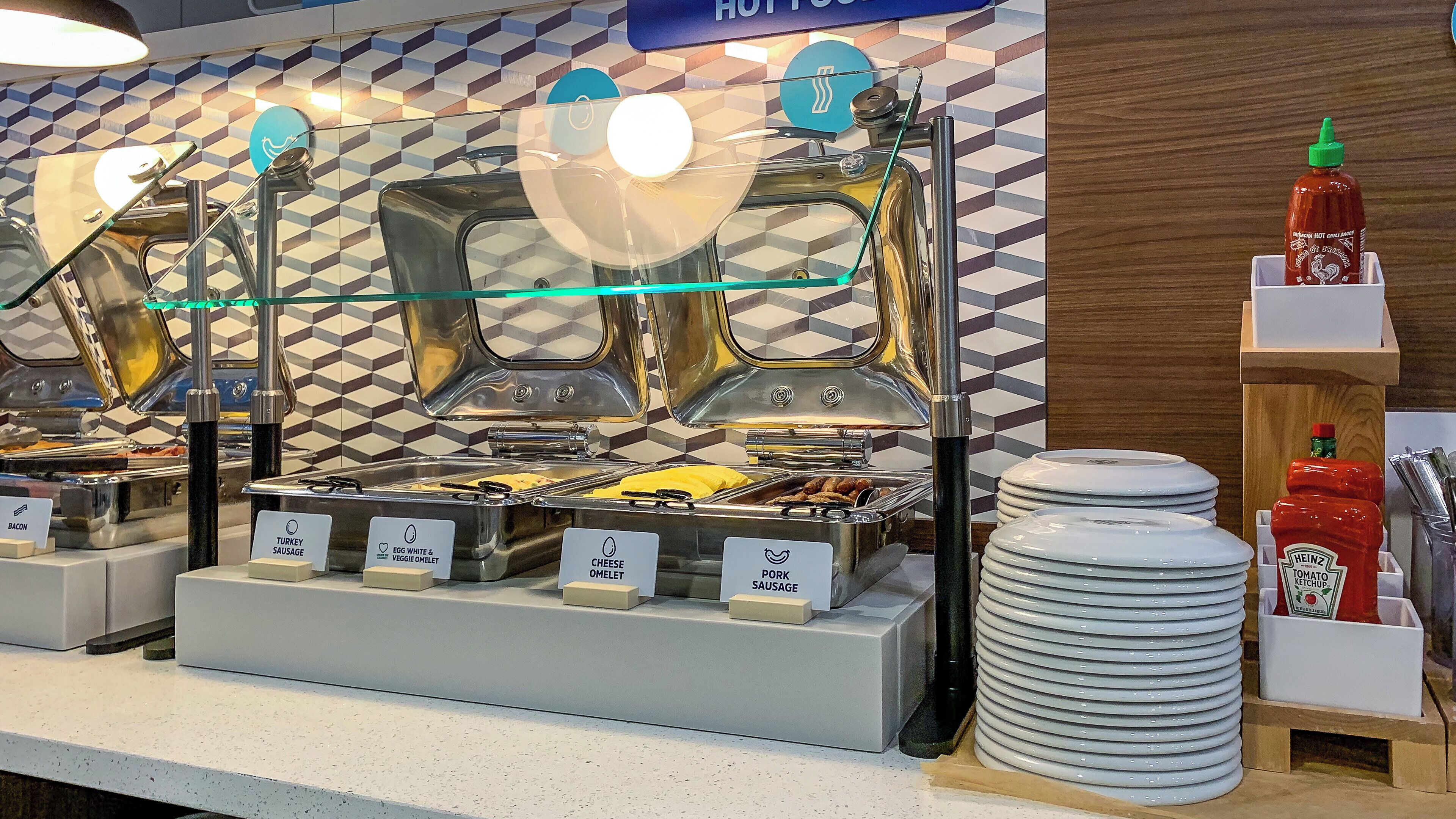 A buffet area with labeled food stations including bacon, turkey sausage, egg white & veggie omelet, cheese omelet, and pork sausage.