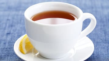 A white cup of tea on a saucer with a lemon slice beside it, placed on a blue textured surface.