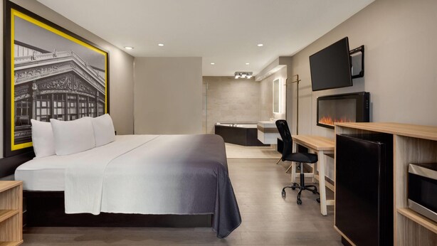 A modern hotel room with a large bed, a desk, a chair, a TV, and a fireplace. - Super 8 by Wyndham Meadowlands (Carlstadt)