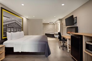 A modern hotel room with a large bed, a desk, a chair, a TV, and a fireplace. - Super 8 by Wyndham Meadowlands (Carlstadt)