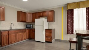 A kitchen with wooden cabinets, a white refrigerator, a microwave, and a dining table with chairs. - Super 8 by Wyndham Meadowlands (Carlstadt)
