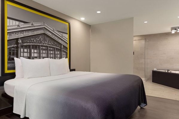 A modern hotel room with a large bed, a glass shower enclosure, and a framed black and white photo on the wall.