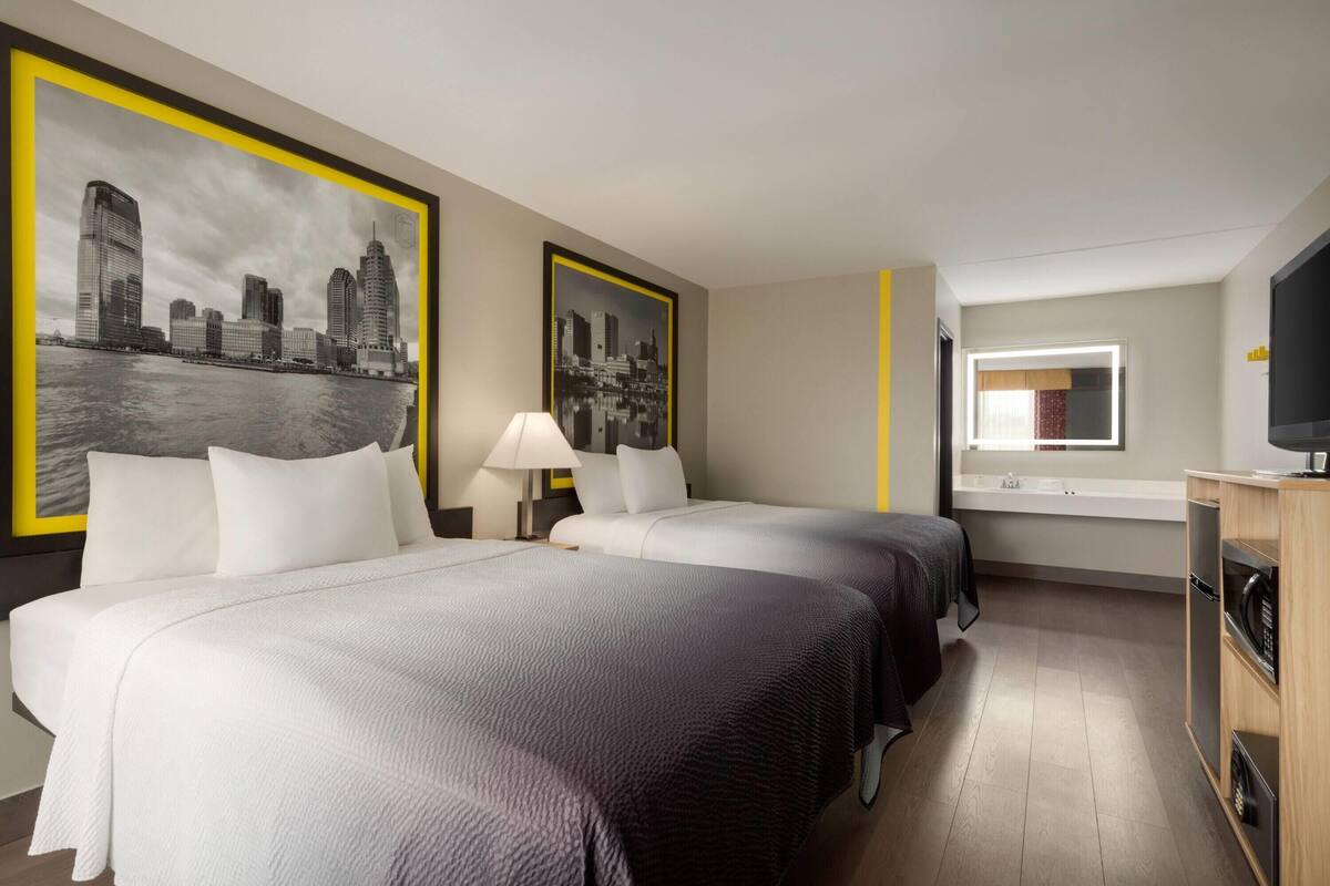 A hotel room with two beds, a TV, a desk, and a window with a view of the cityscape.
