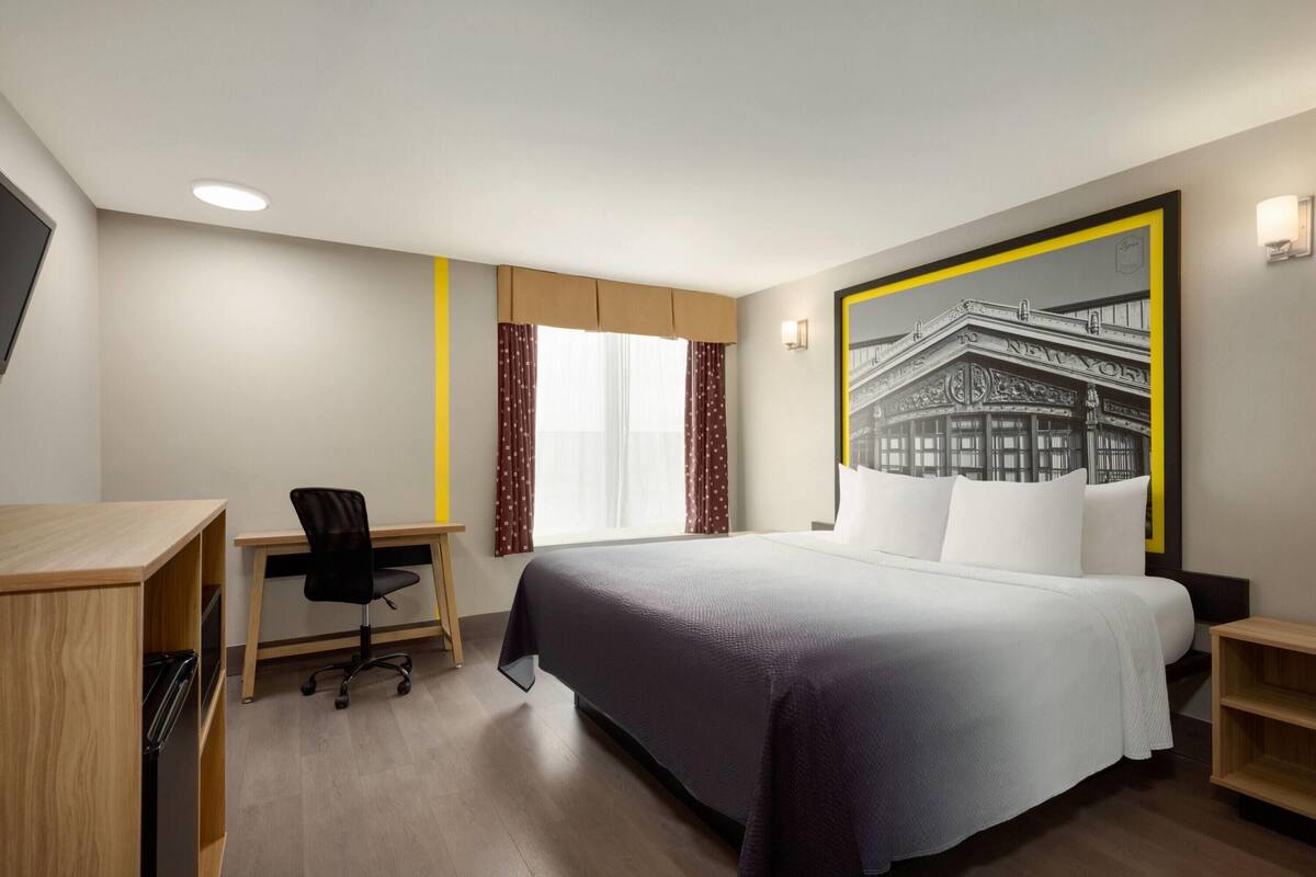 A hotel room with a bed, desk, chair, and a large framed picture on the wall.
