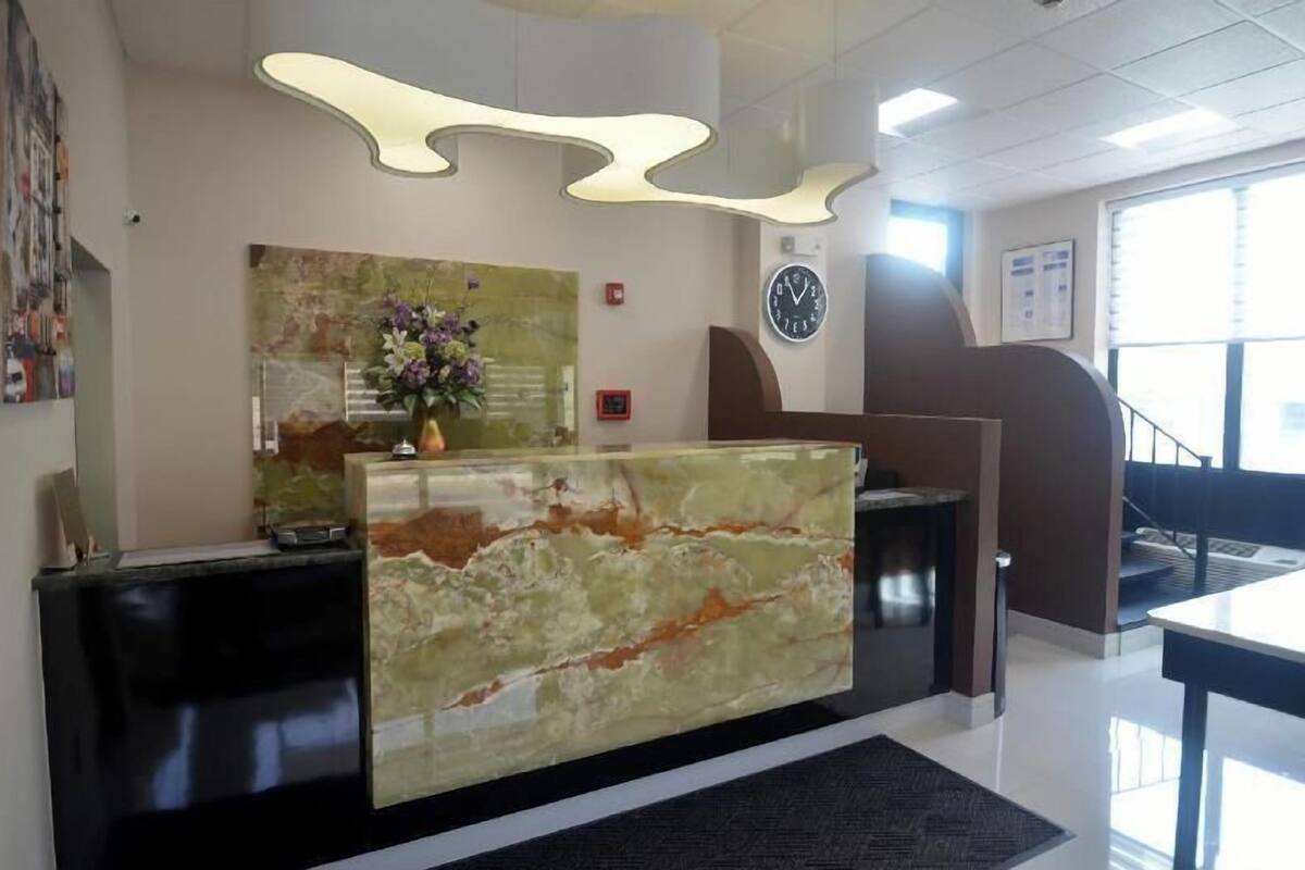 A reception desk with a marble top, a clock on the wall, and a staircase in the background.