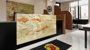 A reception area with a marble counter, abstract art, a clock, and a view of the outside. - Super 8 by Wyndham Meadowlands (Carlstadt)