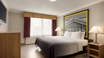 Ein Hotelzimmer mit einem großen Bett, zwei Nachttischen mit Lampen, einem Holznachtkästchen, einem Fenster mit Vorhängen und einem gerahmten Bild an der Wand.