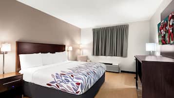A hotel room with a bed, bedside tables, a desk, a chair, a window with curtains, and a flat-screen TV.