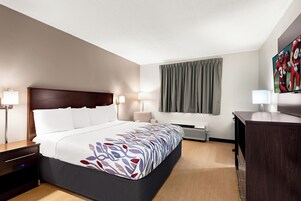 Habitación de hotel con cama, mesitas de noche, escritorio, silla, ventana con cortinas y televisor de pantalla plana.