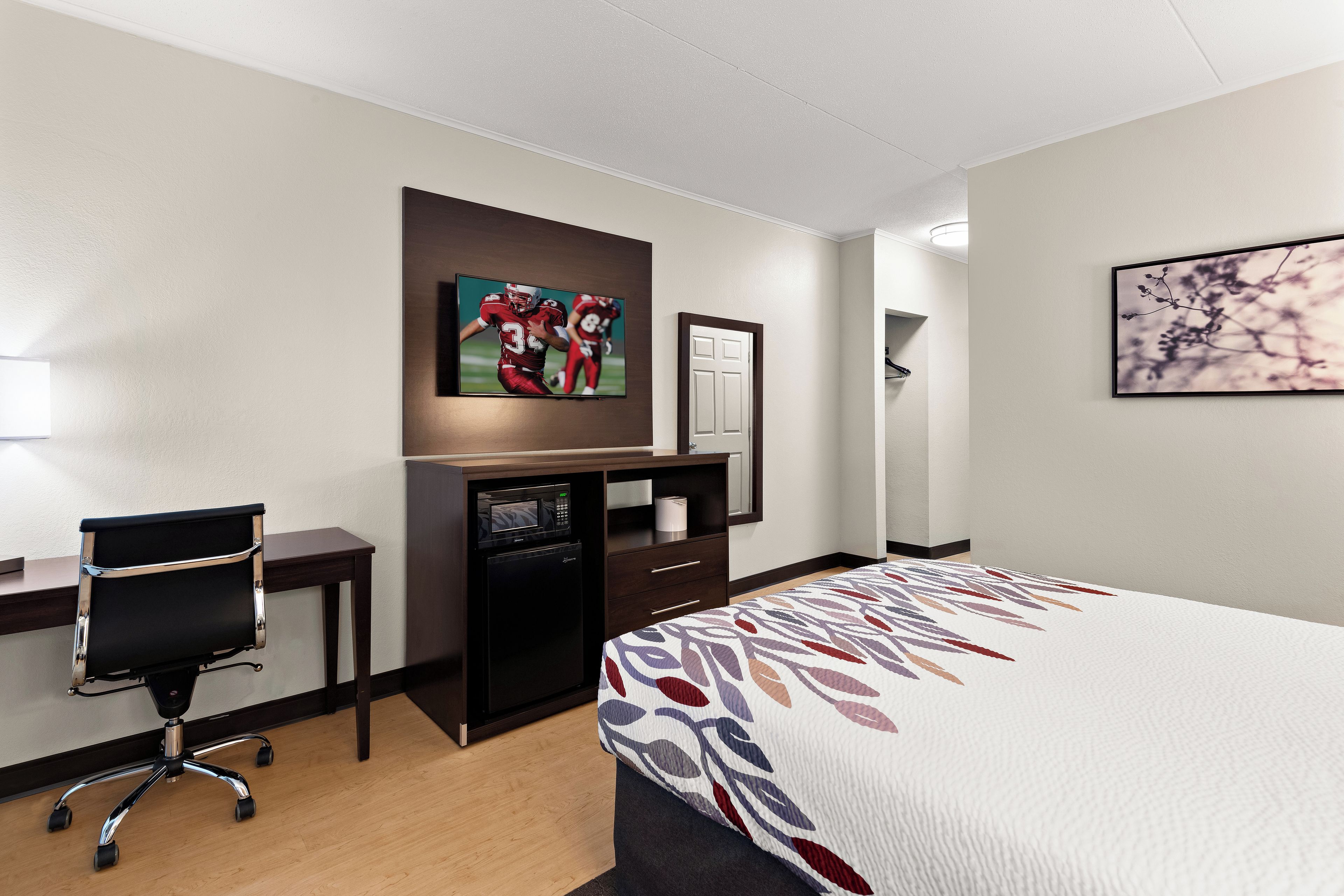 A hotel room with a bed, desk, chair, and a television mounted on the wall.
