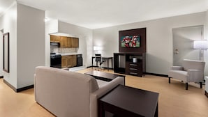 A modern living room with a sofa, a coffee table, a TV mounted on the wall, and a kitchen in the background. - Red Roof Inn Norwich (Norwich)