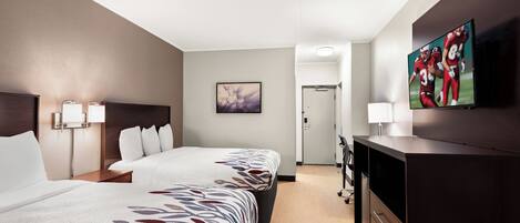 A hotel room with two beds, a desk, a TV, and a door leading to a hallway.
