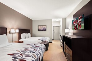 A hotel room with two beds, a desk, a TV, and a door leading to a hallway. - Red Roof Inn Norwich (Norwich)