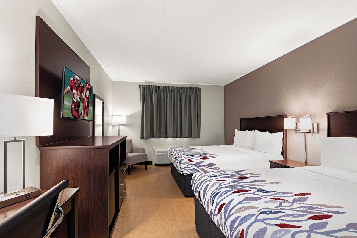 A hotel room with a large bed, a desk with a chair, a TV, and a window with curtains.