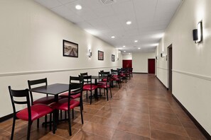 A long corridor with rows of tables and chairs, a red door at the end, and framed pictures on the walls. - Red Roof Inn Norwich (Norwich)