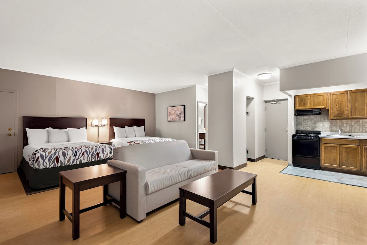 A modern hotel room with a bed, two sofas, a dining table, and a kitchenette.