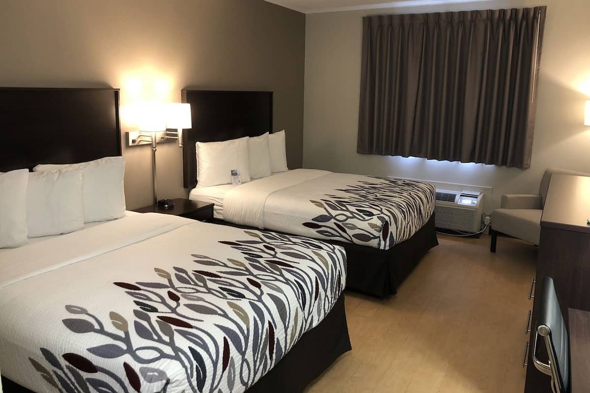 A hotel room with two beds, a desk, a chair, a lamp, and a window with curtains.