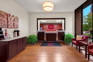 A reception area with a desk, chairs, a coffee machine, and a plant. - Red Roof Inn Norwich (Norwich)