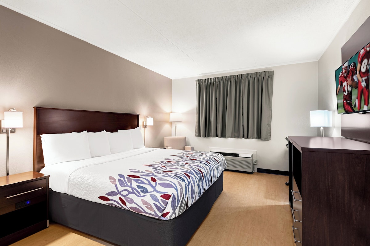 A hotel room with a large bed, bedside tables, a desk, a flat-screen TV, and a window with curtains.