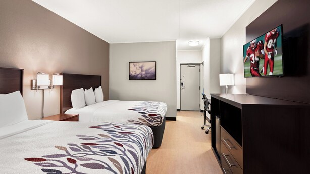 A hotel room with two beds, a TV, a desk, and a door leading to a bathroom. - Red Roof Inn Norwich (Norwich)