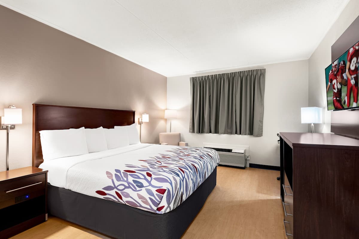 A hotel room with a large bed, bedside tables, a desk, a flat-screen TV, and a window with curtains.