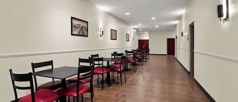 Corredor de hotel com fileiras de mesas e cadeiras, piso de azulejos e uma porta vermelha ao fundo.