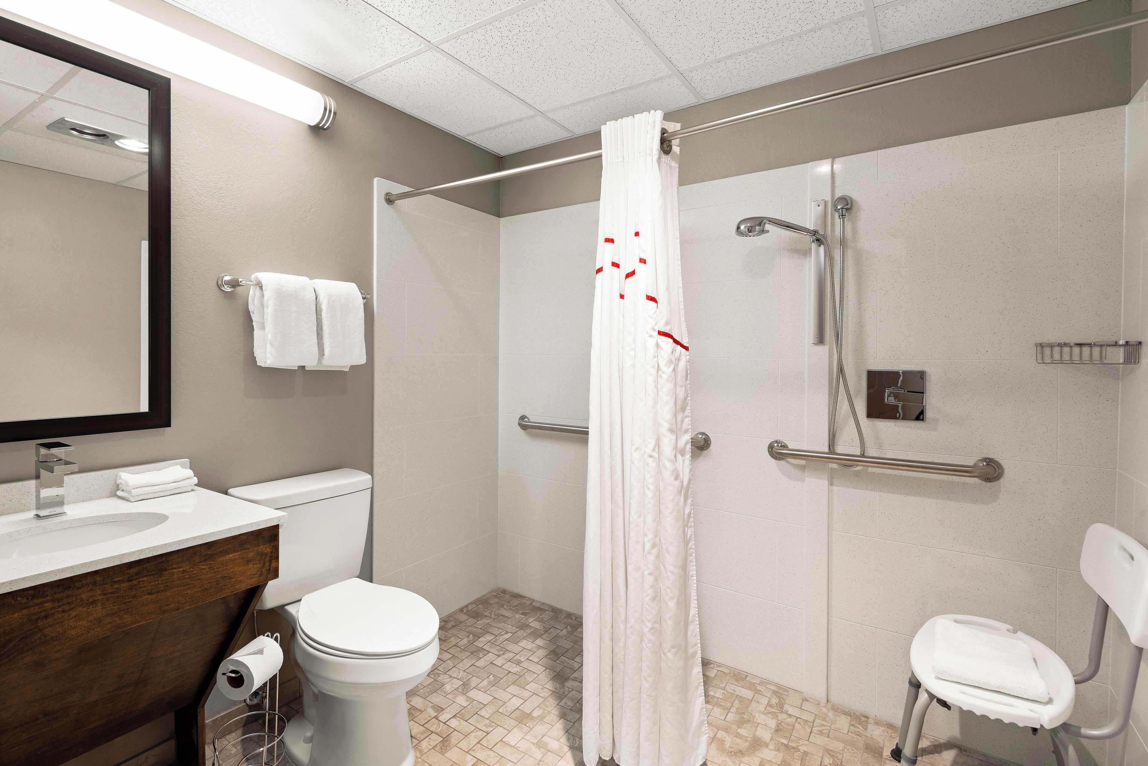 Ein modernes Badezimmer mit Toilette, Waschbecken, Spiegel, Dusche und Haltegriffen.