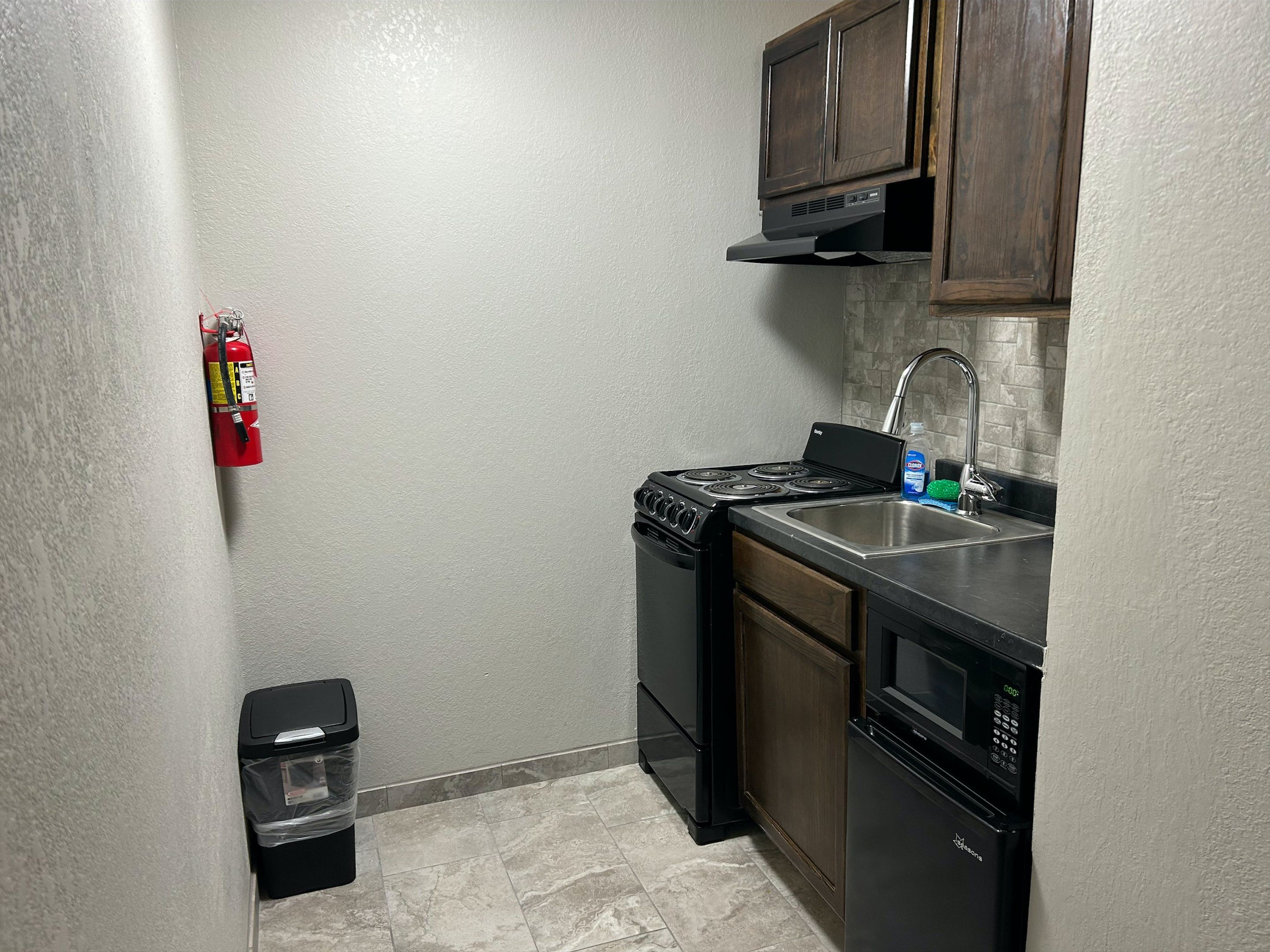 A compact kitchen with a stove, sink, and microwave. A fire extinguisher is mounted on the wall.
