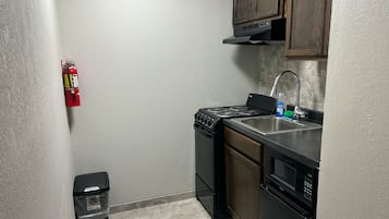 A compact kitchen with a stove, sink, and microwave. A fire extinguisher is mounted on the wall.