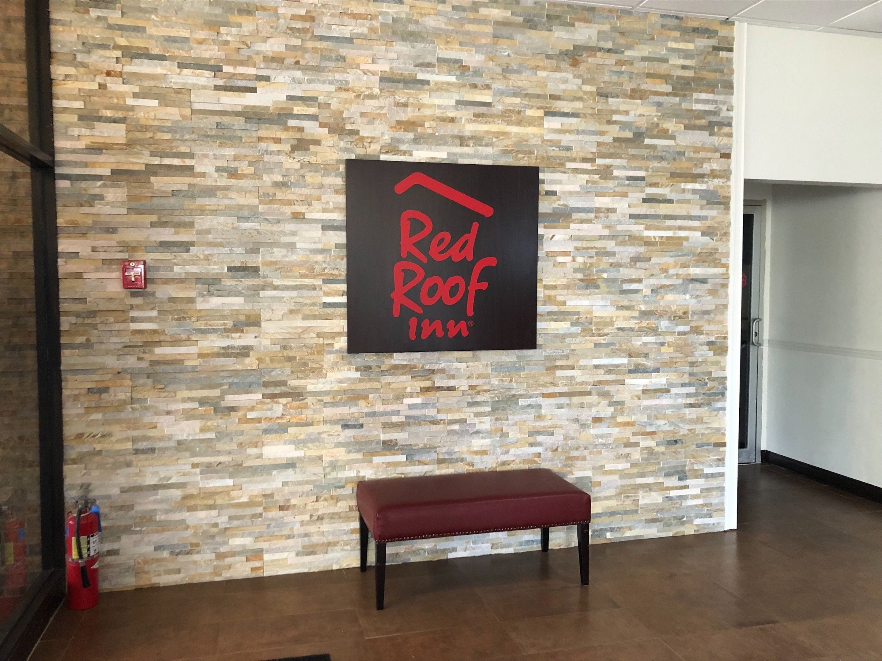 A Red Roof Inn sign on a textured stone wall, a bench, and a fire extinguisher.