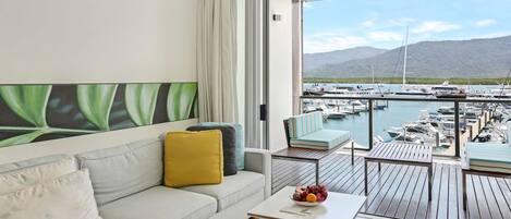 A modern living room with a sofa, a coffee table with fruit, and a view of a marina with boats.