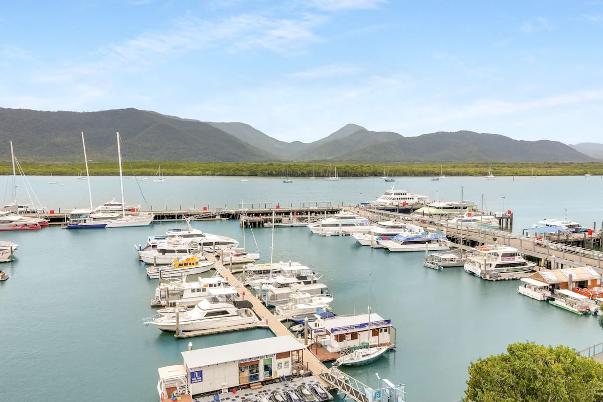 Un puerto deportivo con barcos amarrados, un muelle y montañas al fondo.