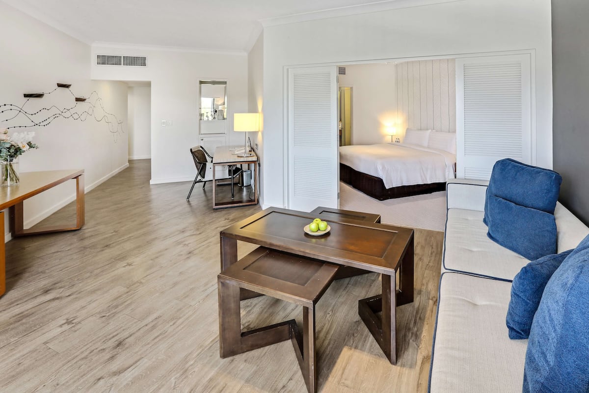Una habitación de hotel con suelo de madera, un escritorio con silla, una cama con ropa blanca y un sillón azul.