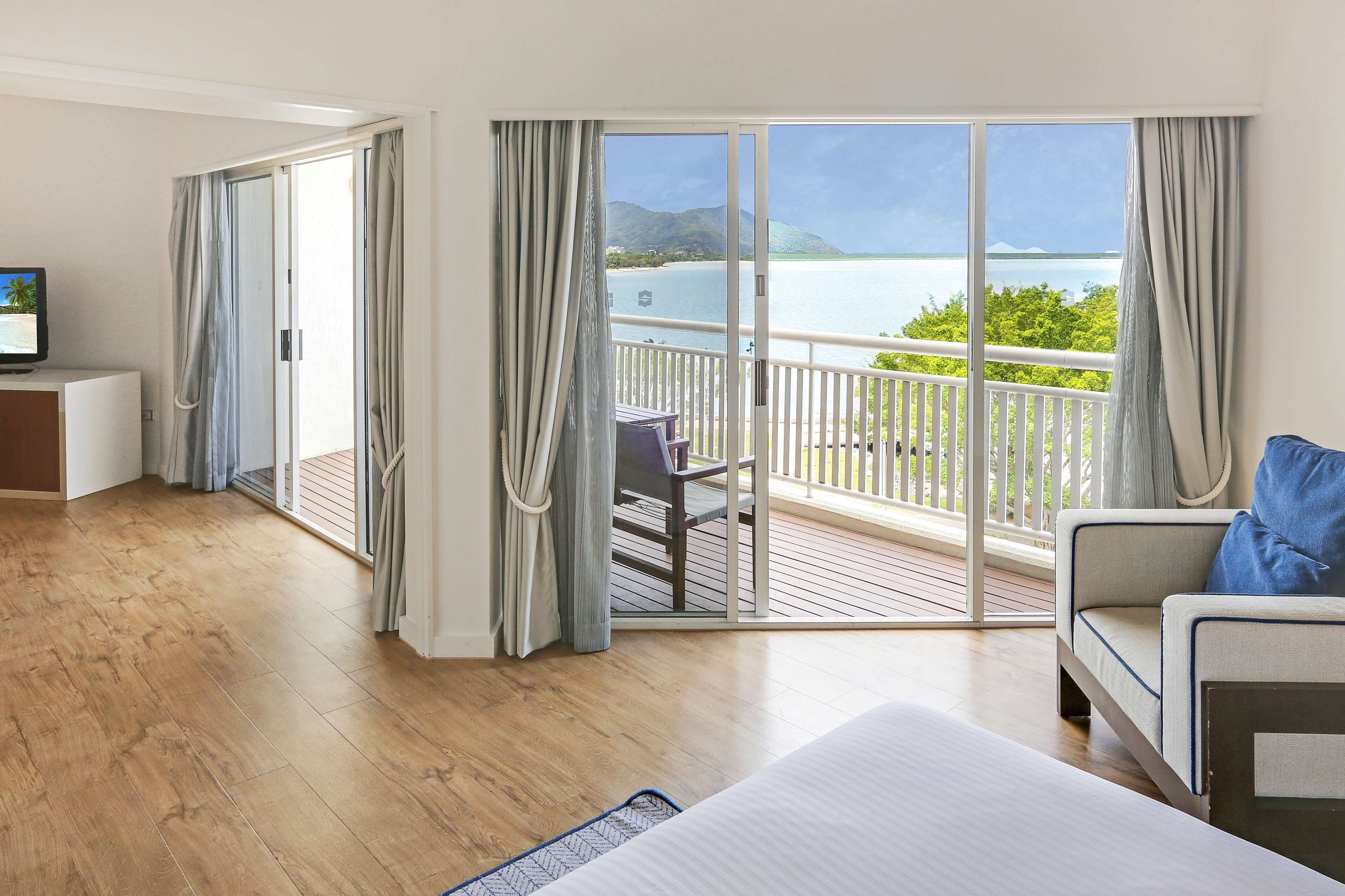 Une chambre d’hôtel avec un balcon, un plancher en bois, un lit, un canapé et un téléviseur posé sur un meuble.