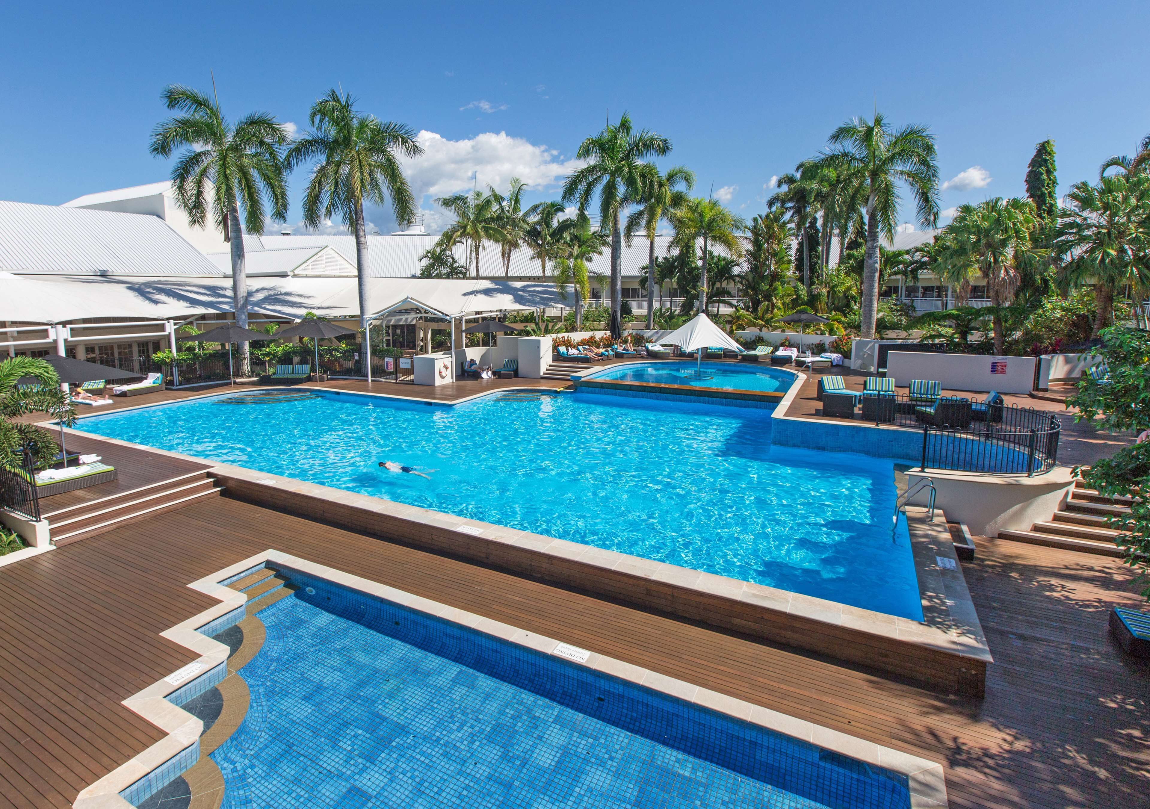 A large outdoor swimming pool with multiple lanes, surrounded by palm trees and lounge chairs.