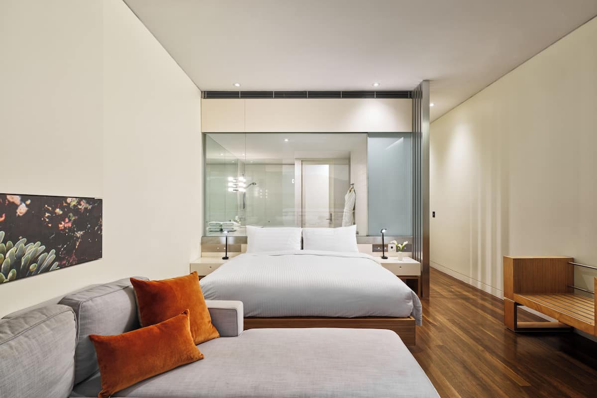 Un dormitorio moderno con una cama grande, un sofá gris y un banco de madera.