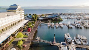 Un puerto deportivo con varias embarcaciones amarradas, un puente peatonal y un edificio grande con techo azul.