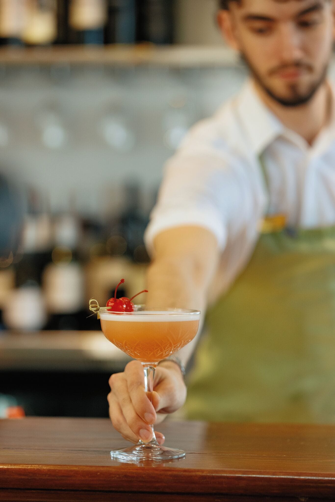 A bartender holding a cocktail glass with a cherry garnish.