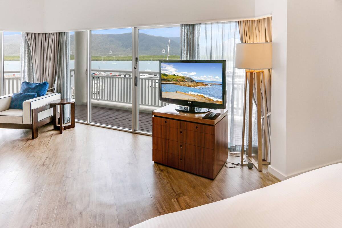 Habitación de hotel con televisor grande, muebles de madera, balcón con vista al mar y una lámpara.