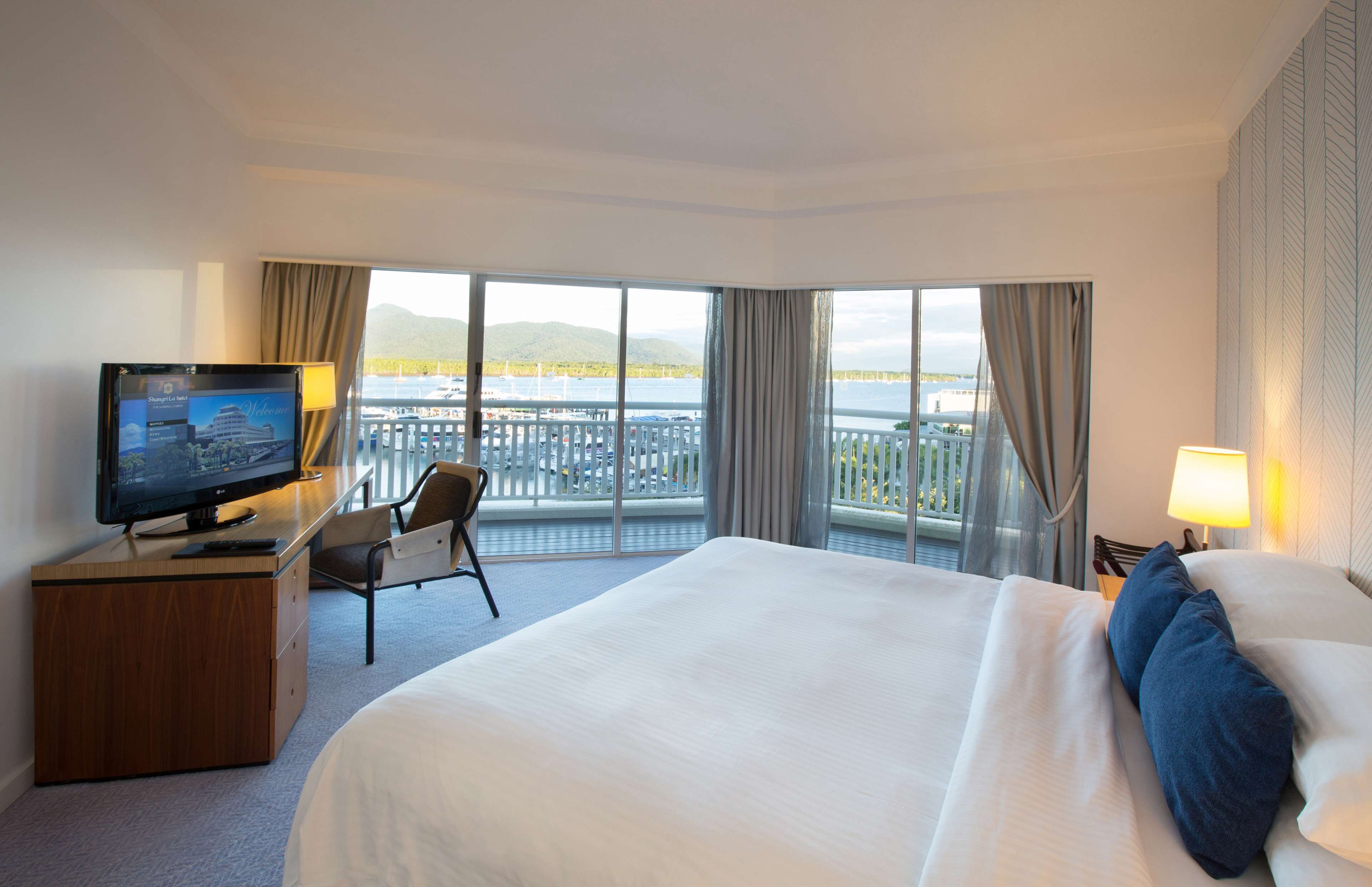 Une chambre d’hôtel avec un grand lit, un bureau avec une télévision, une chaise et une vue sur le bord de l’eau.