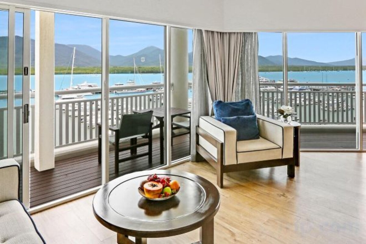 A room with a balcony, a dining table with a plate of food, and a sofa with a cushion.