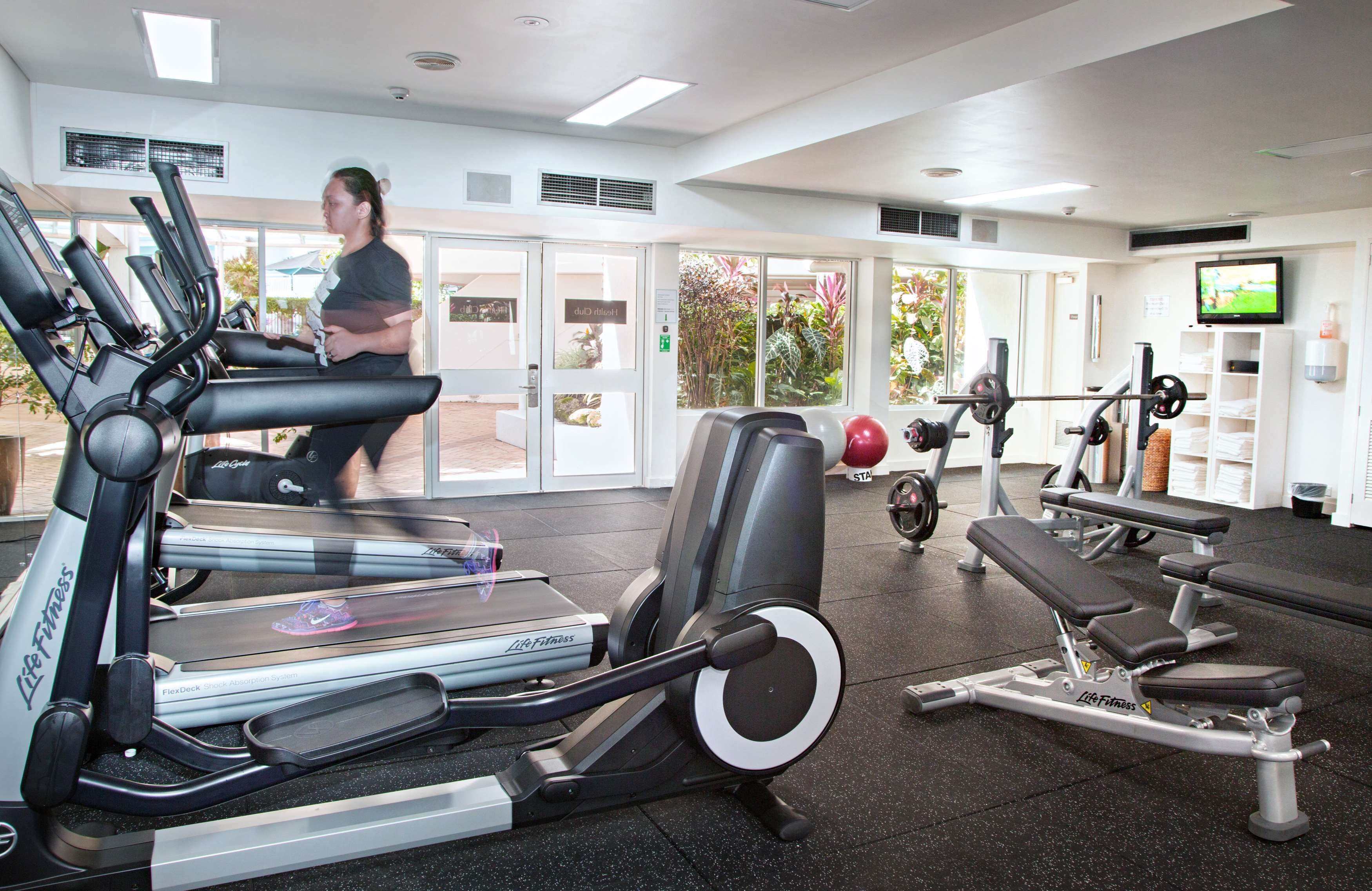 A gym with treadmills, weight machines, and a TV screen.