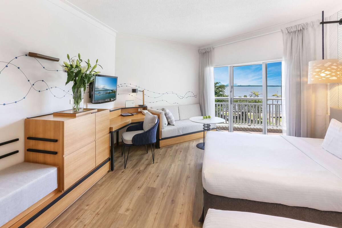Habitación de hotel moderna con una cama, un escritorio con ordenador, una silla, un sofá y un balcón con vistas al mar.