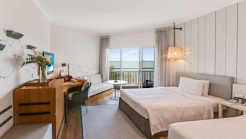 A hotel room with two beds, a desk, a chair, a small table, and a balcony with a view.