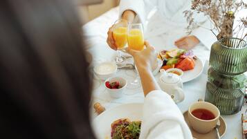 A breakfast setting with a table set for two, including plates of food, a cup of tea, and a glass of orange juice.