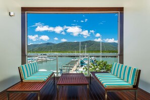 A balcony with wooden flooring, two striped sofas, and a small table. It overlooks a marina with boats and a mountainous landscape. - Shangri-La The Marina, Cairns (Cairns)
